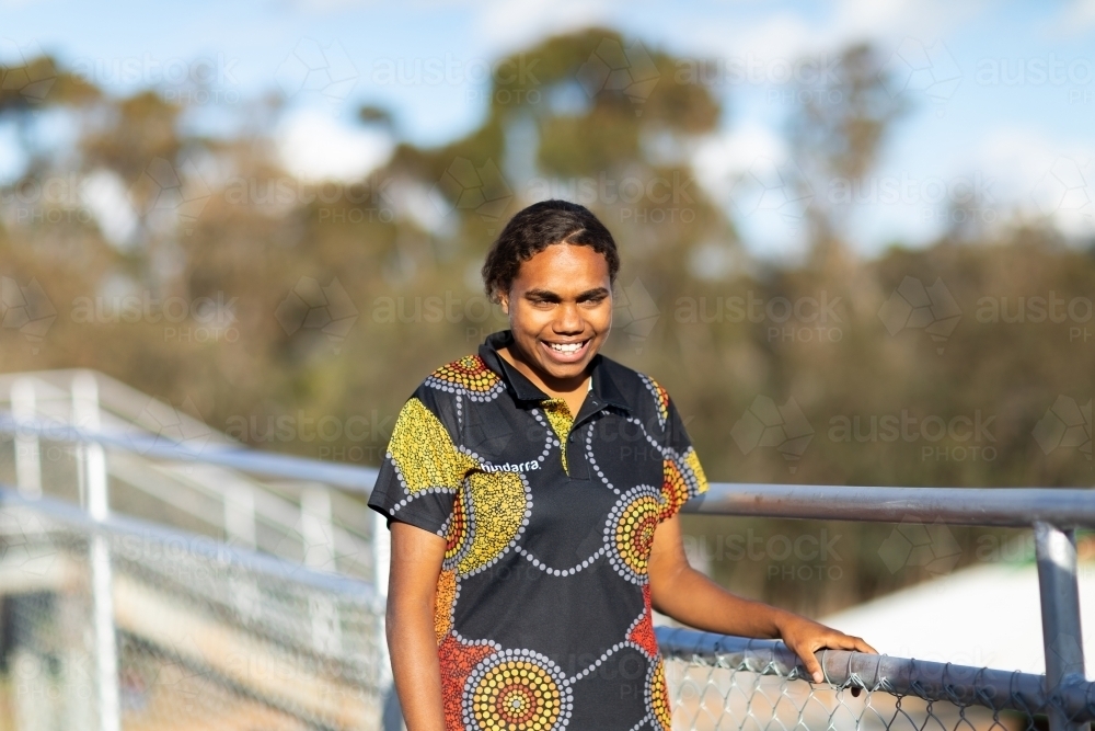 smiling young woman holding handrail with trees in background - Australian Stock Image
