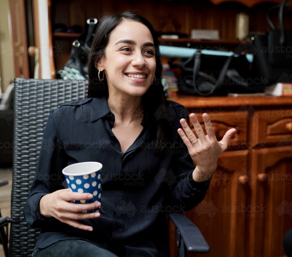 Smiling Young Woman Inside Holding a Cup in Hand - Australian Stock Image