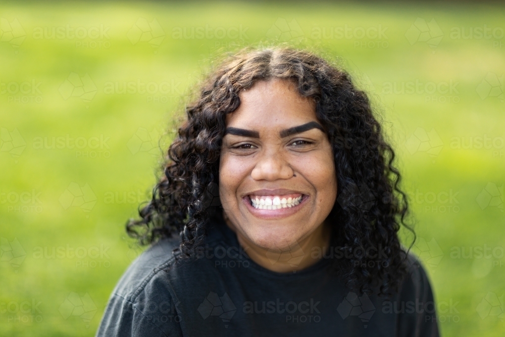 smiling young woman wearing black against green grass background - Australian Stock Image