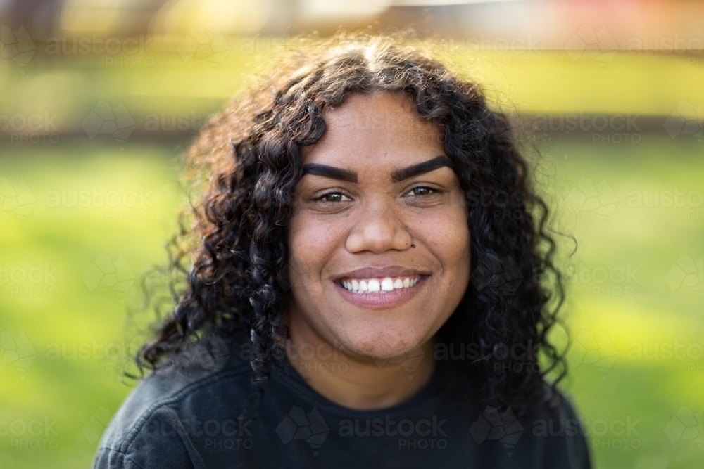 smiling young woman wearing black against green grass background - Australian Stock Image
