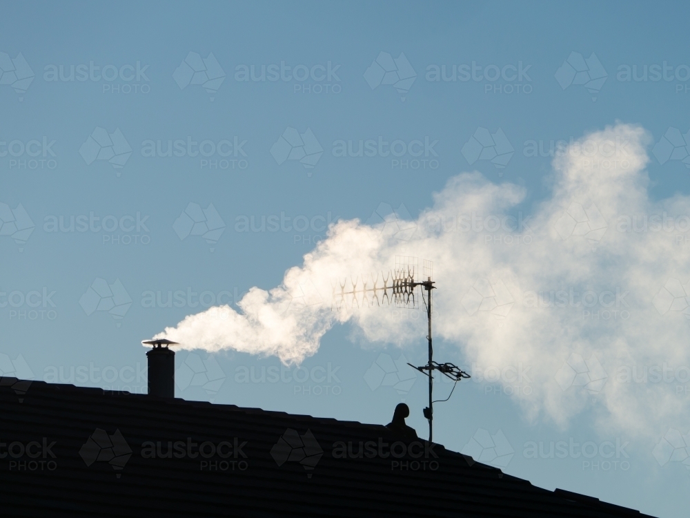 Smoke billowing from a chimney through a TV aerial against a blue sky - Australian Stock Image