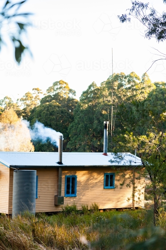 Smoke coming from chimney in cabin in clearing - Australian Stock Image