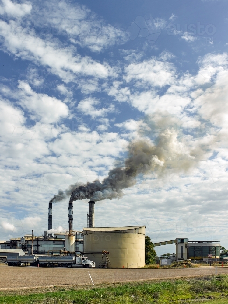 Smoke pouring from smoke stacks at a regional sugar refinery - Australian Stock Image