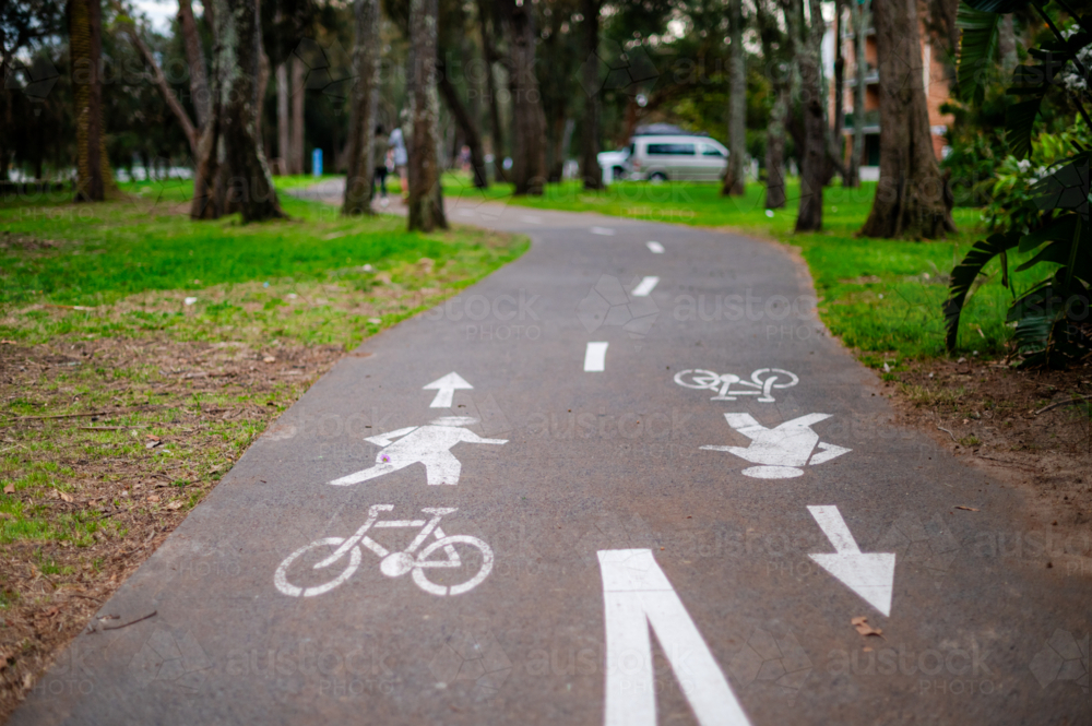 Smooth footpath divides bike and pedestrian lanes, surrounded by trees in a peaceful park. - Australian Stock Image