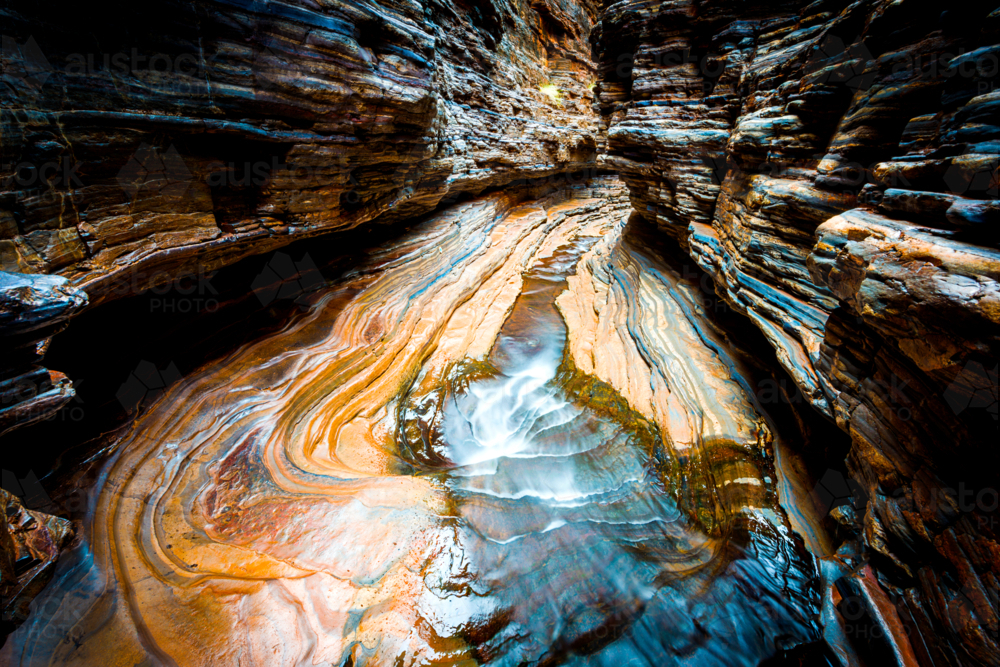 Smooth water flows through the banded rock layers of a gorge - Australian Stock Image
