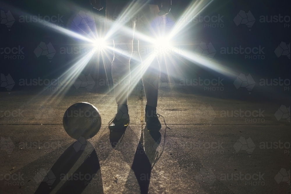 Soccer player standing in front of headlights at night - Australian Stock Image