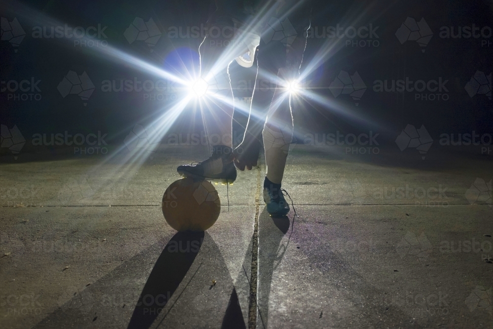 Soccer player standing in front of headlights at night - Australian Stock Image