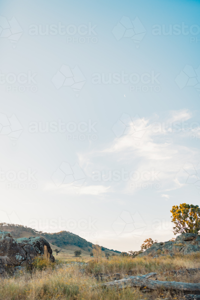 Soft blue sky over rural Australian landscape with rocks and trees - Australian Stock Image