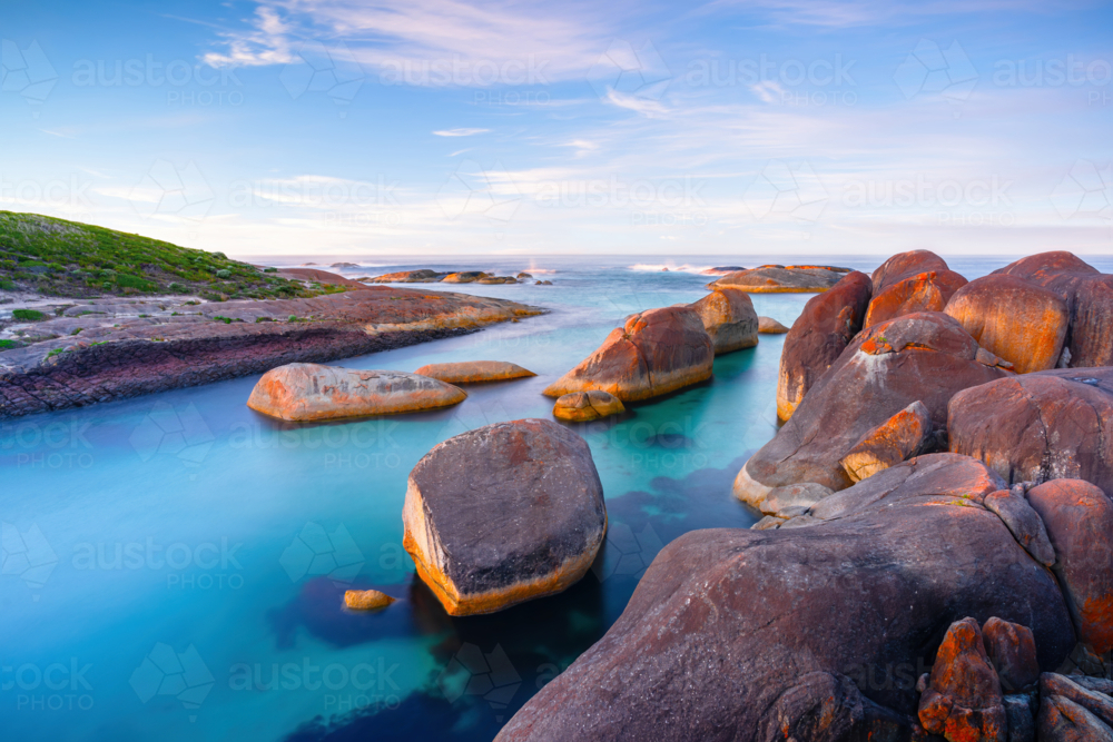 Soft evening light washes over the granite boulders and turquoise waters of Elephant Rocks - Australian Stock Image