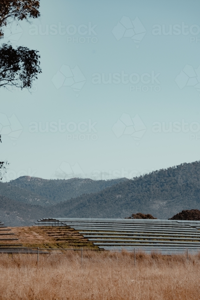 Solar farm panels on a hill for renewable energy with mountains in the background. - Australian Stock Image