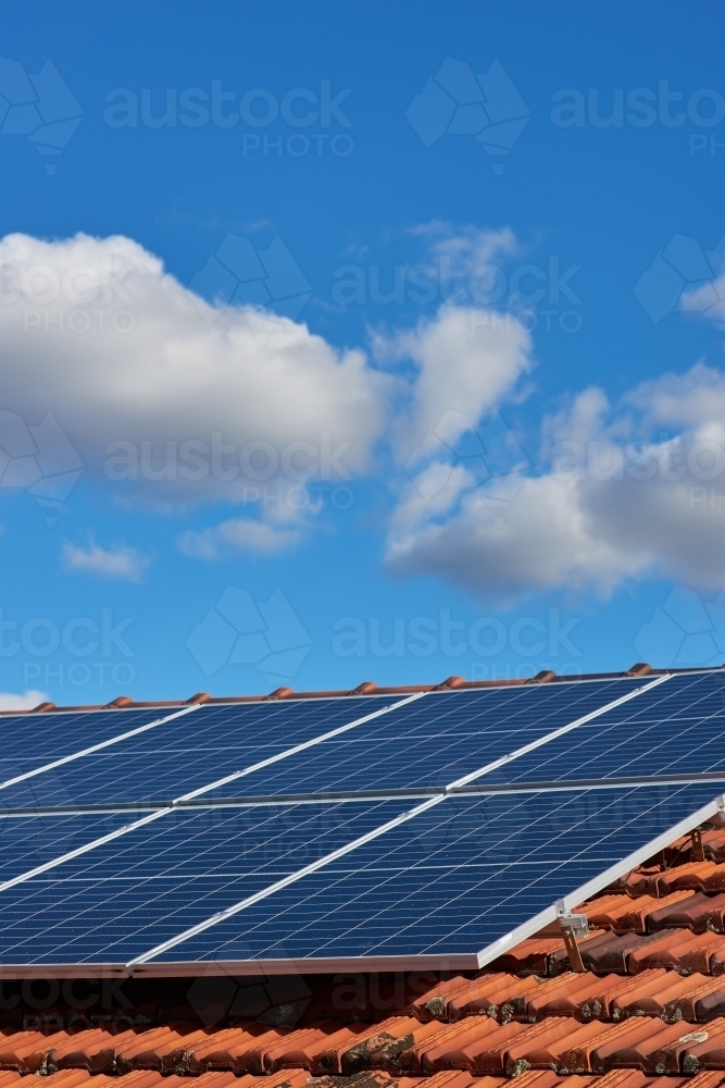 Solar panels on a tile roof under blue sky with clouds - Australian Stock Image