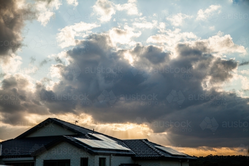 Solar panels on house roof with sunset and clouds behind - Australian Stock Image