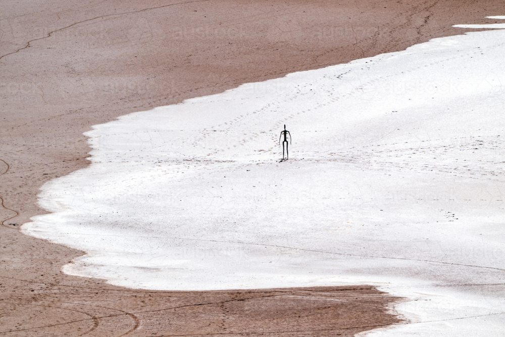 Solitary metal figure standing on a vast salt-crusted lakebed. - Australian Stock Image