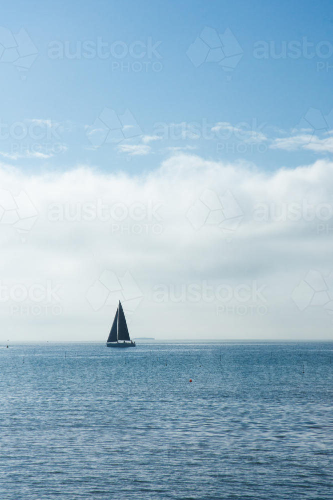 Solo yacht on calm ocean with blue sunny sky - vertical - Australian Stock Image