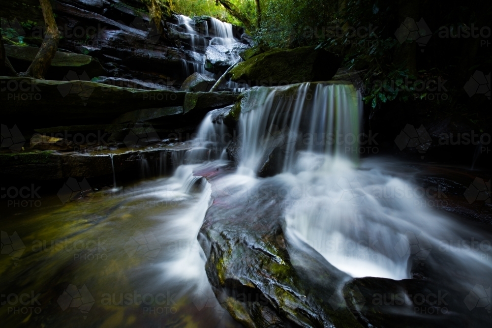 Somersby Falls, long exposure of mossy waterfall in dark green forest - Australian Stock Image