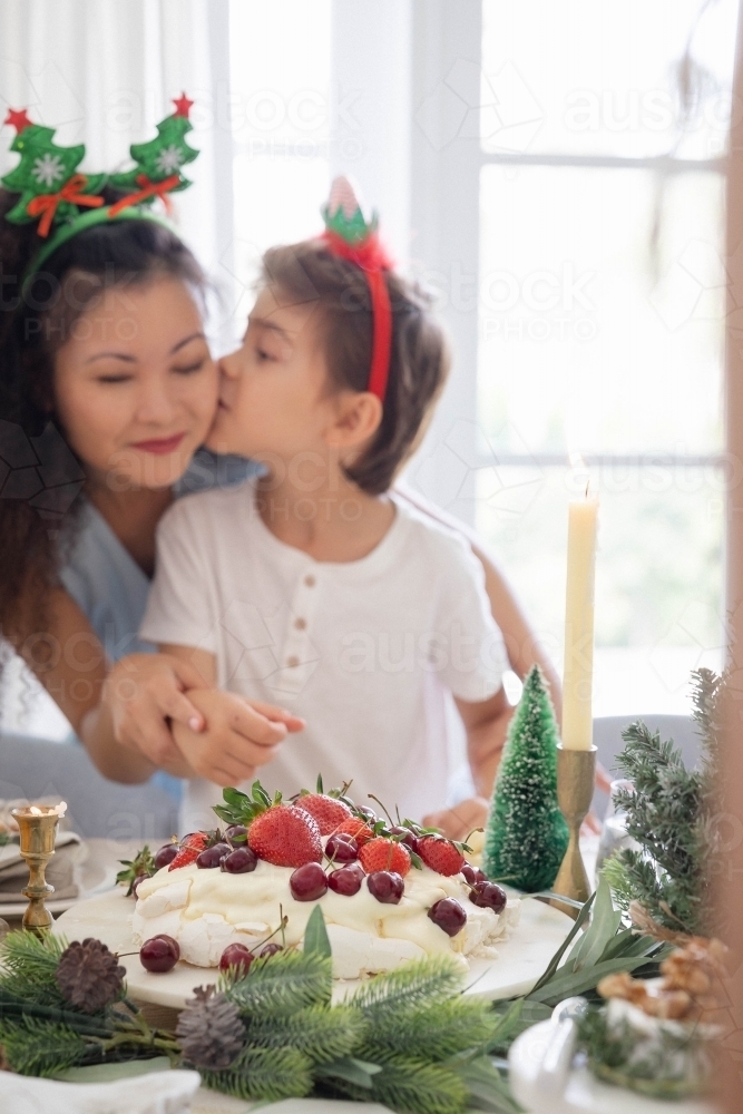 Son kissing mum on the cheek at Christmas themed table - Australian Stock Image