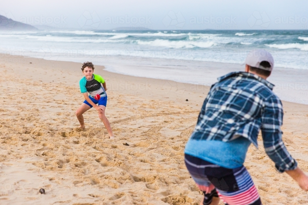 Son throwing ball to father on beach playing cricket - Australian Stock Image