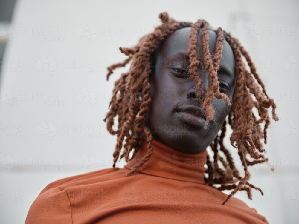 South Sudanese man wearing orange turtleneck looking down - Australian Stock Image