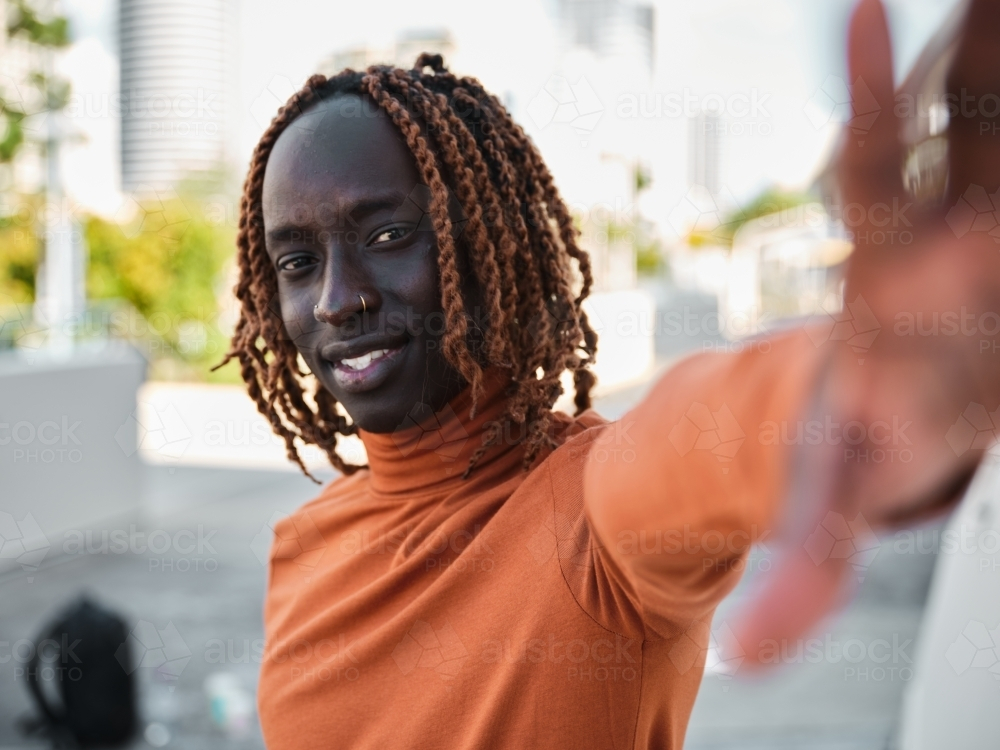 South Sudanese man wearing orange turtleneck reaching his hand out - Australian Stock Image