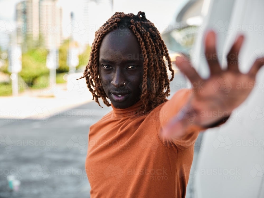 South Sudanese man wearing orange turtleneck reaching his hand out - Australian Stock Image