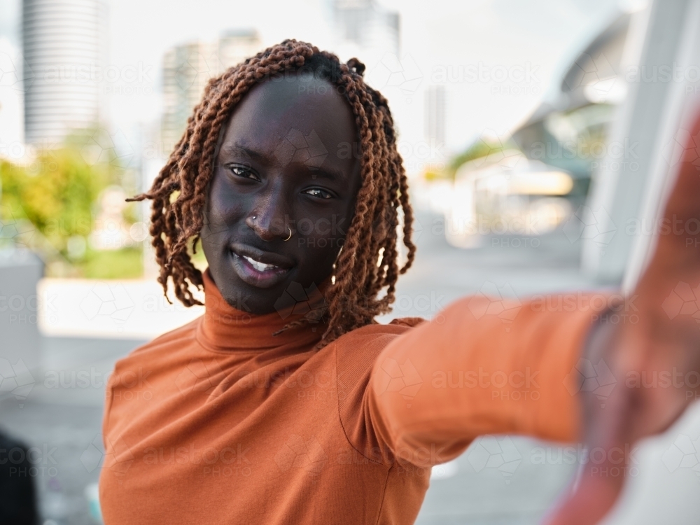 South Sudanese man wearing orange turtleneck reaching towards the camera - Australian Stock Image