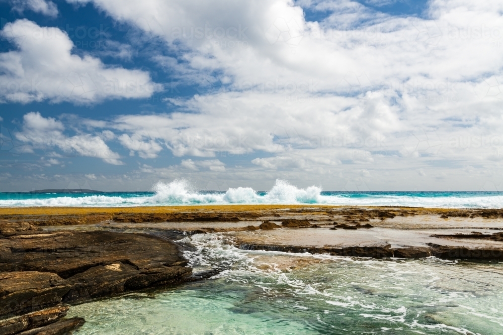Spectacular view of water flowing into rock pools with surf crashing behind and dramatic sky - Australian Stock Image