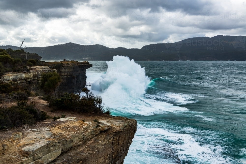 Spectacular waves crashing against cliffs in stormy ocean swell. - Australian Stock Image