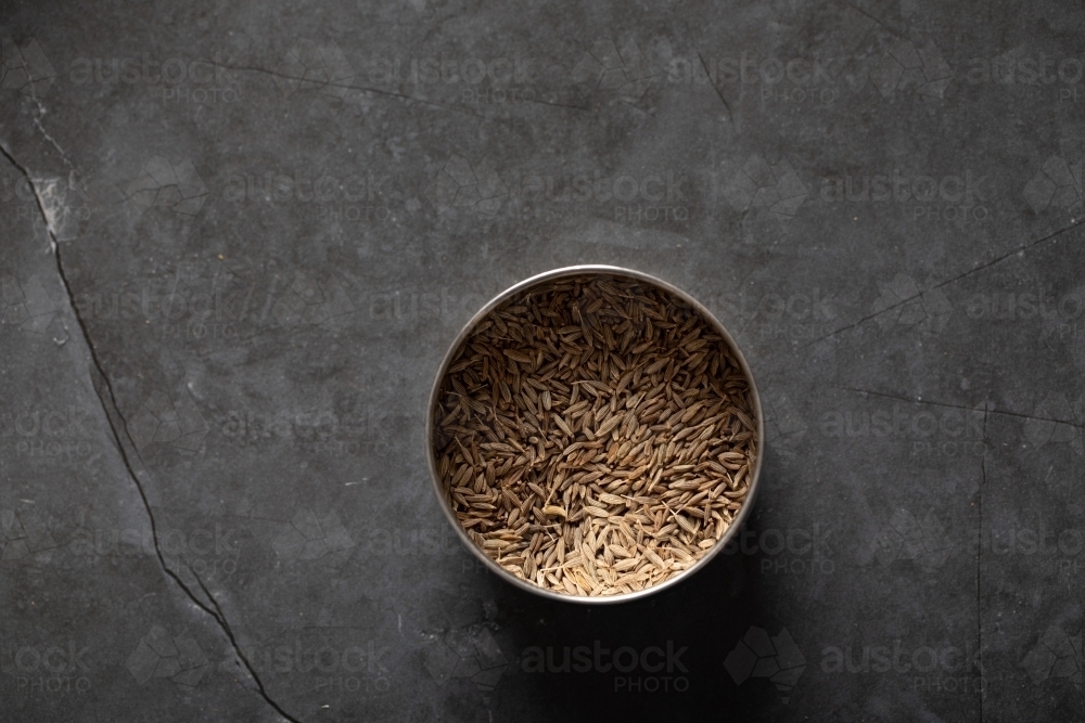 Spice tin of cumin seeds on dark marble background - Australian Stock Image