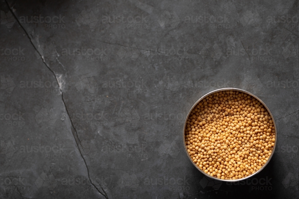 Spice tin of yellow mustards seeds on dark marble background - Australian Stock Image