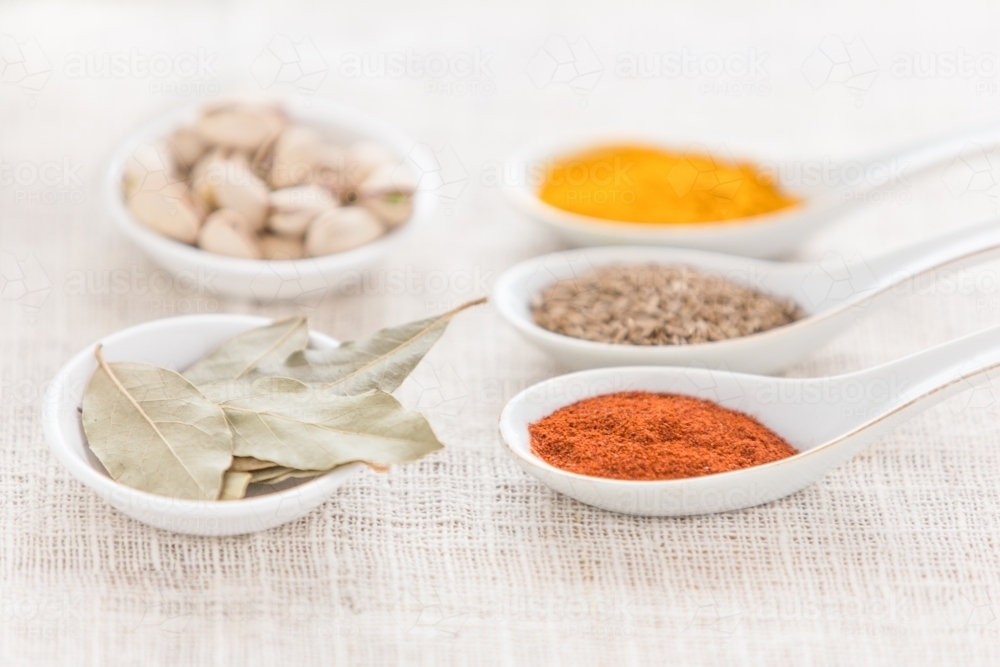 spices, nuts and bay leaves in white spoons on white cloth - Australian Stock Image