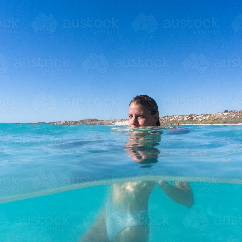 Image of Split shot underwater view of woman floating in turquoise