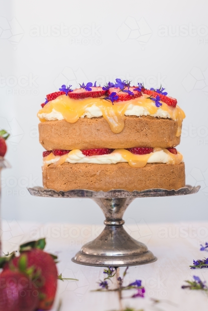 sponge cake with lemon curd, strawberries and edible flowers on a vintage cake stand - Australian Stock Image