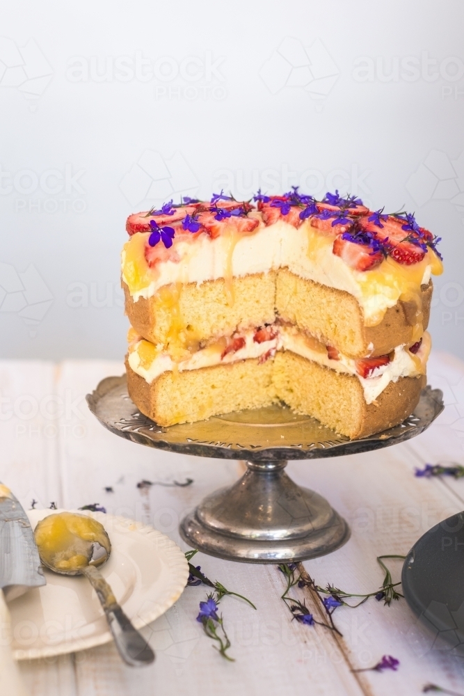 sponge cake with lemon curd, strawberries and edible flowers with pieces cut out - Australian Stock Image