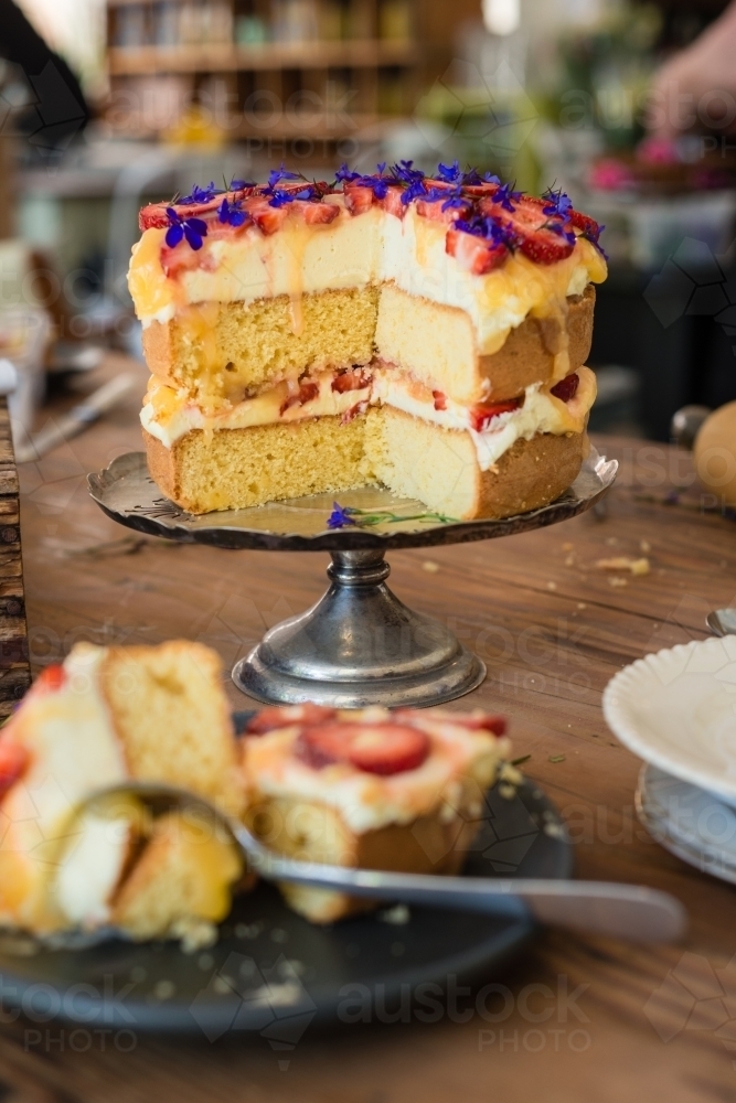 sponge cake with lemon curd, strawberries and edible flowers with pieces cut out - Australian Stock Image