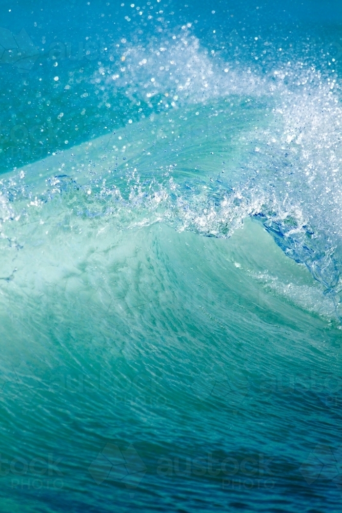 Spray flies as a wave is curling before breaking. - Australian Stock Image