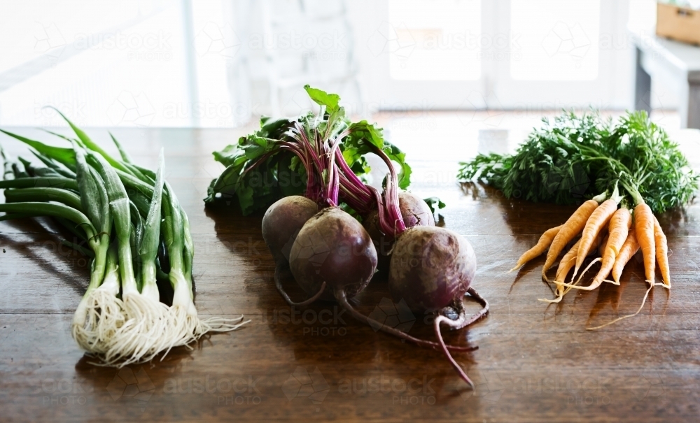 Spring onions, beetroot and carrots on a wooden kitchen bench - Australian Stock Image