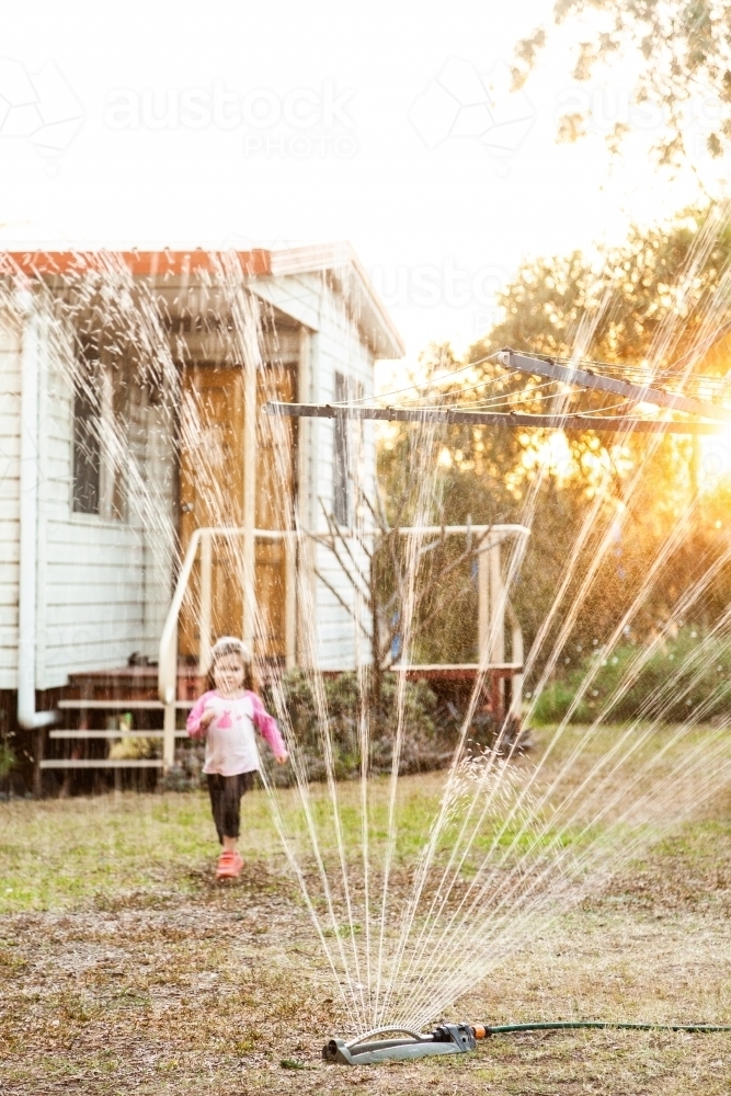 Sprinkler and garden hose watering dry lawn in the backyard - Australian Stock Image