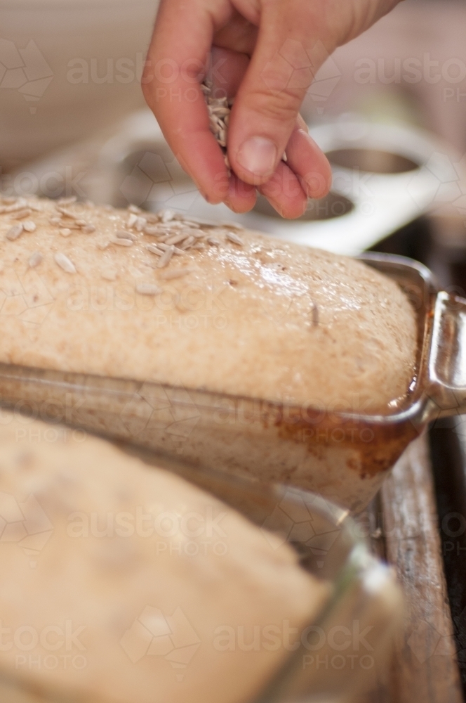 Sprinkling seeds onto home baked bread - Australian Stock Image
