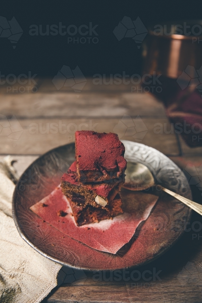 Stack of freshly baked red dusted chocolate brownies on timber surface with dark background - Australian Stock Image