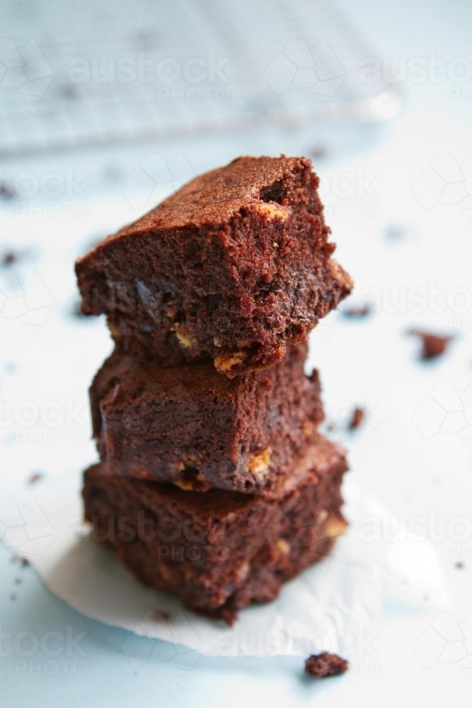 Stack of homemade chocolate brownies on pastel blue background - Australian Stock Image