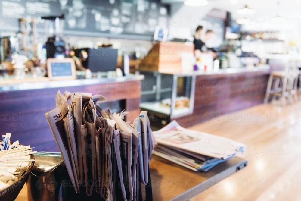 Stack of newspapers in cafe with service area in background - Australian Stock Image