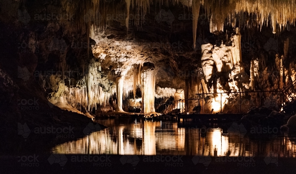 Stalactites and Stalagmites over a lake within a cave - Australian Stock Image