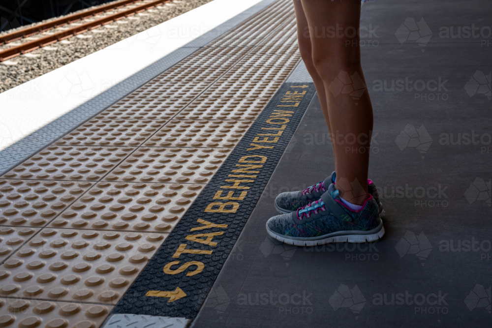 Stand behind the yellow line, girl in sneakers standing on a train platform - Australian Stock Image