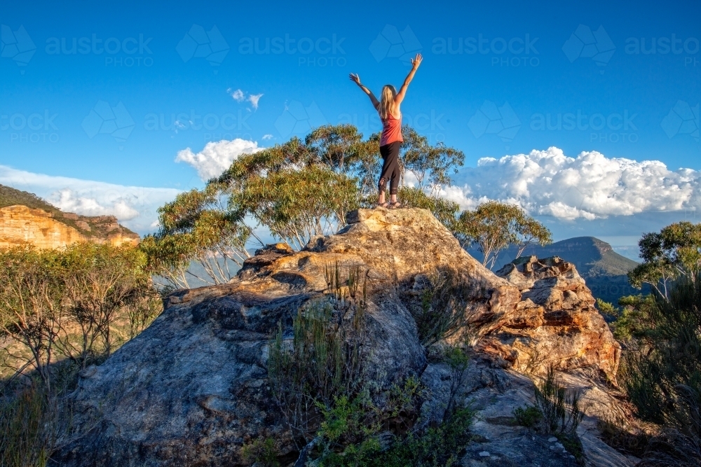 Standing at the top of the rocky peak arms outstretched in awe, success, challenge,achievement. - Australian Stock Image