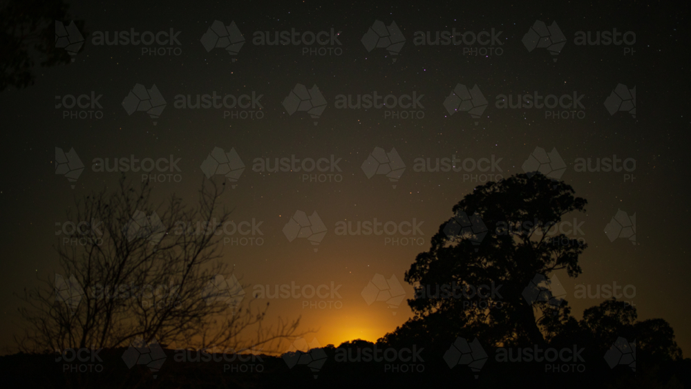 Starlit sky over rural Australian landscape with golden glow of rising moon beneath the horizon - Australian Stock Image