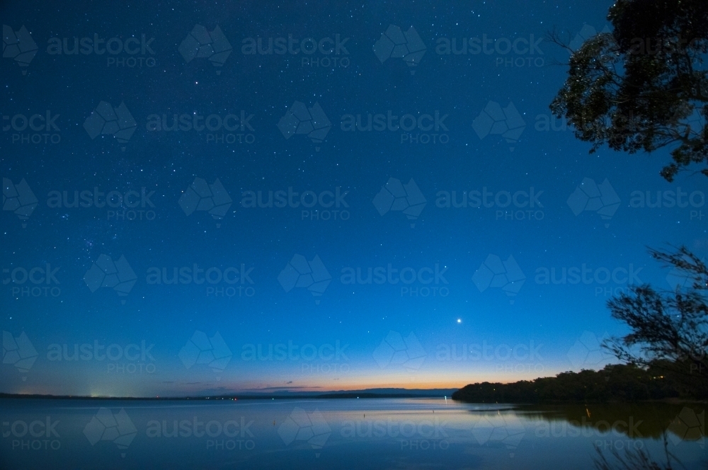 Stars in a blue night sky over water - Australian Stock Image