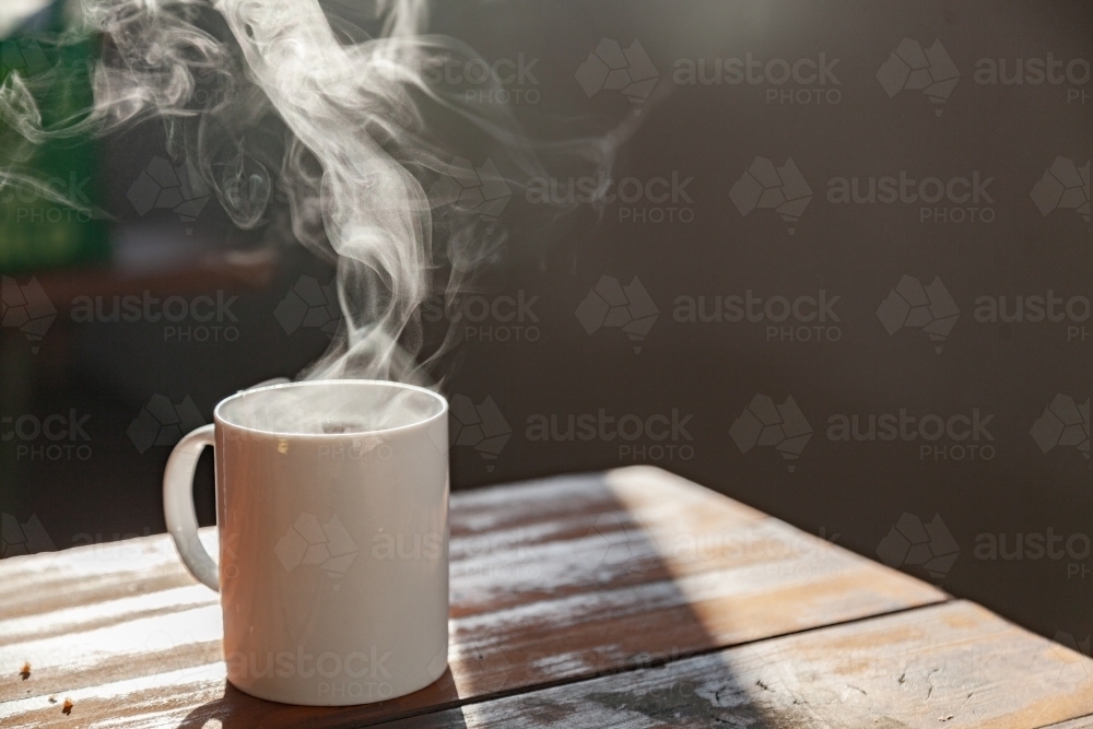 Steam from hot mug of tea on picnic bench in the morning light - Australian Stock Image