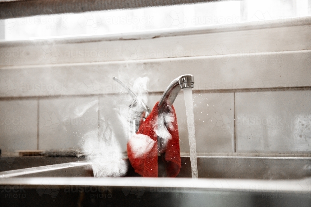 Steam from hot washing up water running into kitchen sink from tap - Australian Stock Image