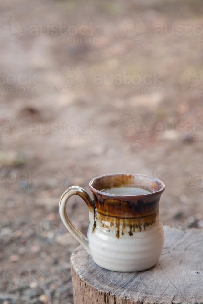 Steaming mug sitting on a stump on a cold morning - Australian Stock Image