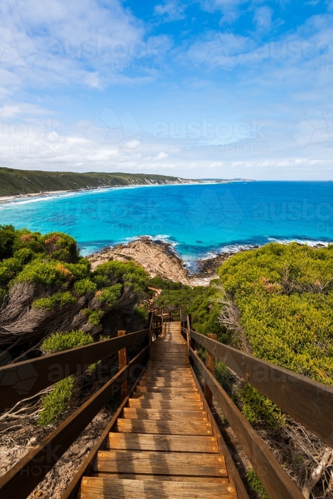 Steps leading down to rocks and colourful ocean  with sweeping views of coastline in portrait - Australian Stock Image